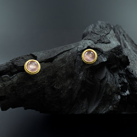 DIVAMAS pink Monalisa stone stud earrings with a gold bezel setting, displayed on a dark textured background._01
