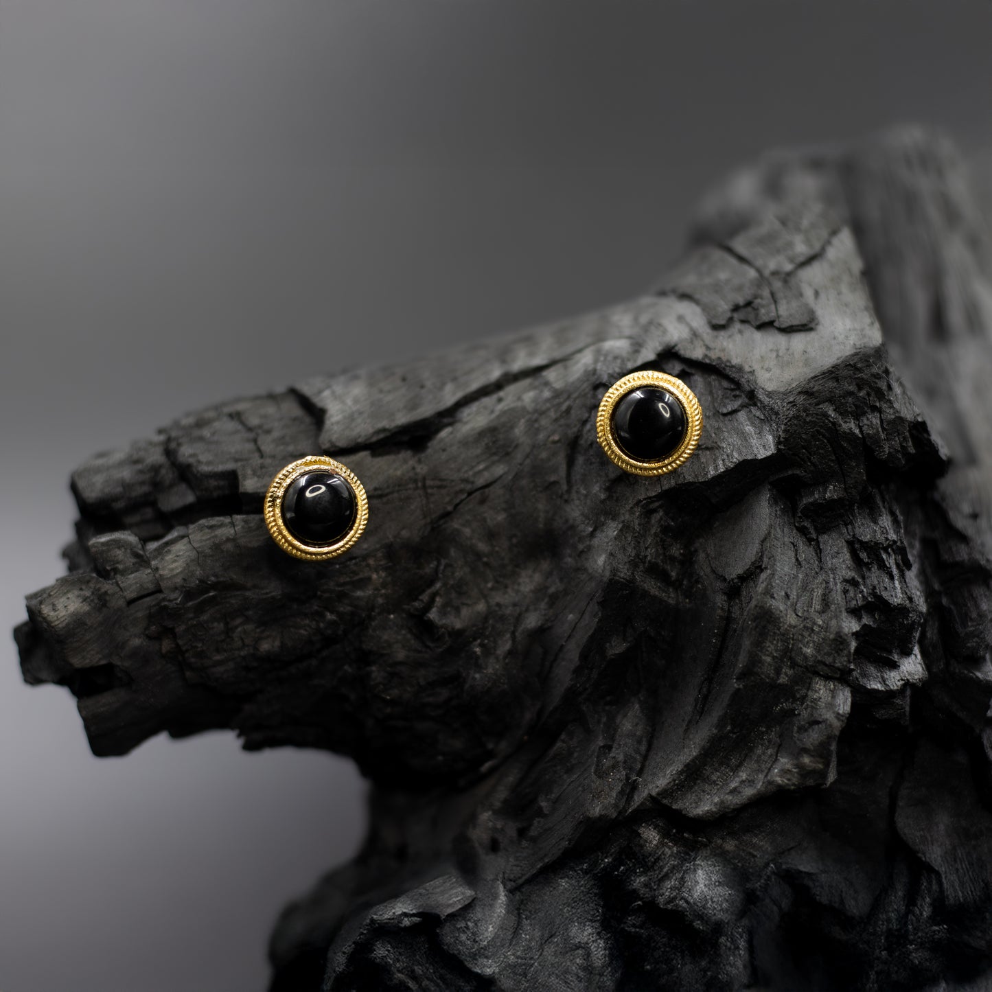 DIVAMAS black Monalisa stone stud earrings with a glossy sheen and elegant gold trim, set on a dramatic dark background._01