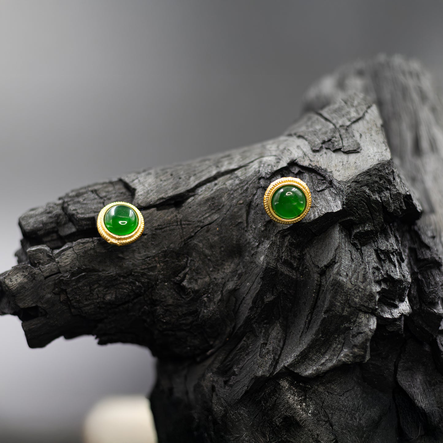 DIVAMAS green Monalisa stone stud earrings featuring a luminous stone framed in gold, shown on a dark surface._01